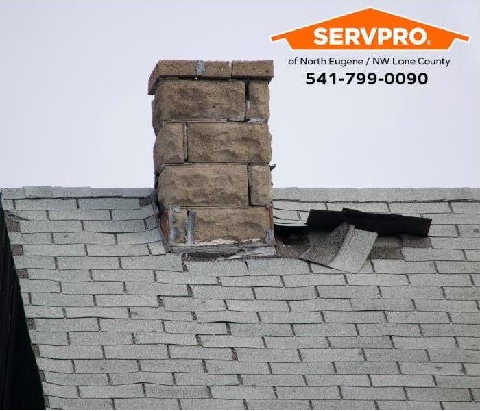 A chimney with missing caulking, torn flashing, and missing roof shingles is shown. 